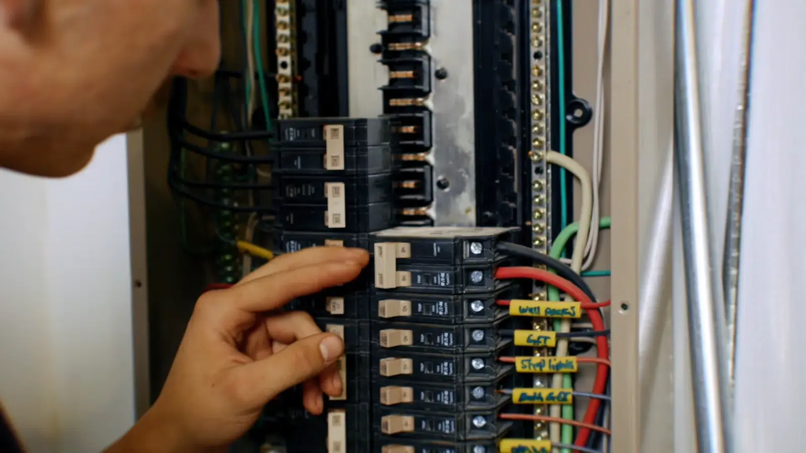 Technician inspecting a residential circuit breaker panel with labeled breakers and colored wiring during electrical service in St. George